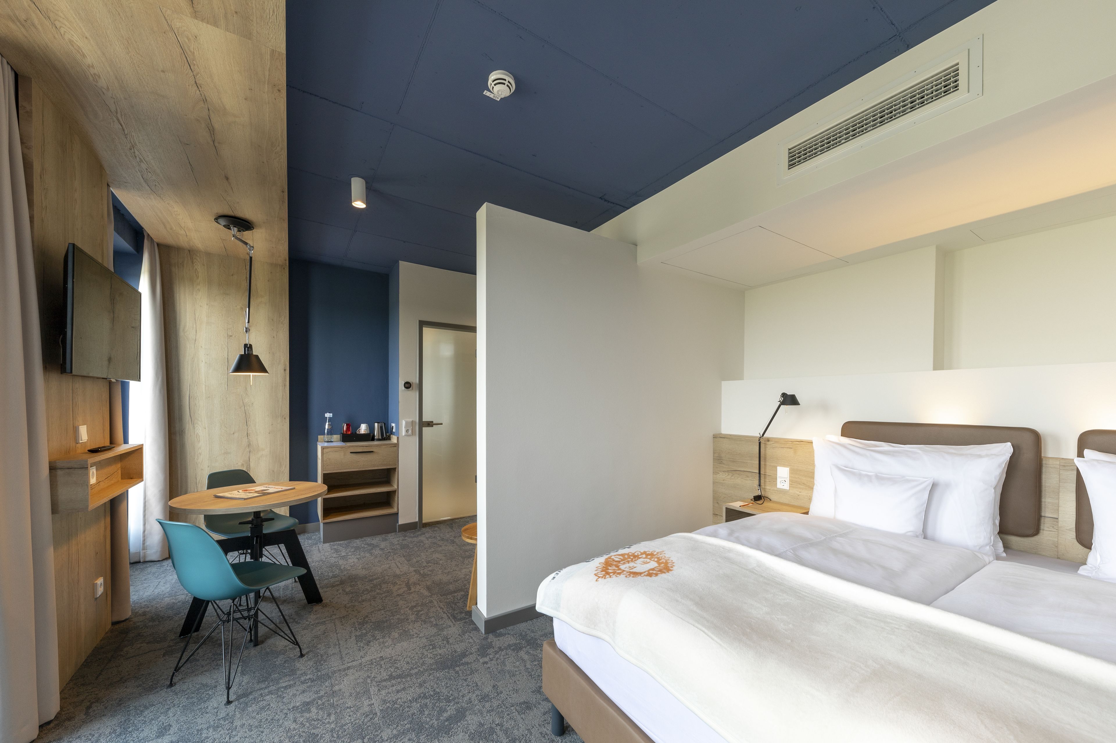 Habitación de hotel con una cama, un escritorio y una silla. Se ve una puerta que da a otra habitación.