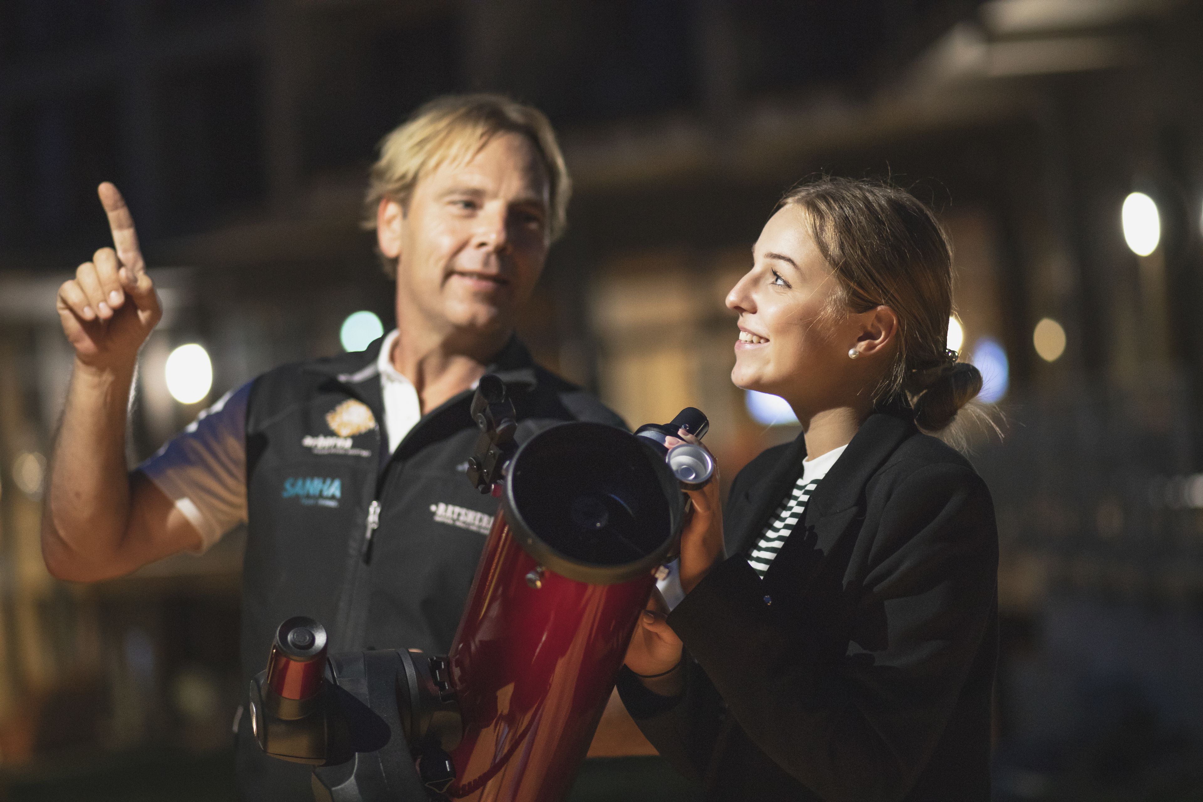 Two people holding telescopes, one pointing upwards.
