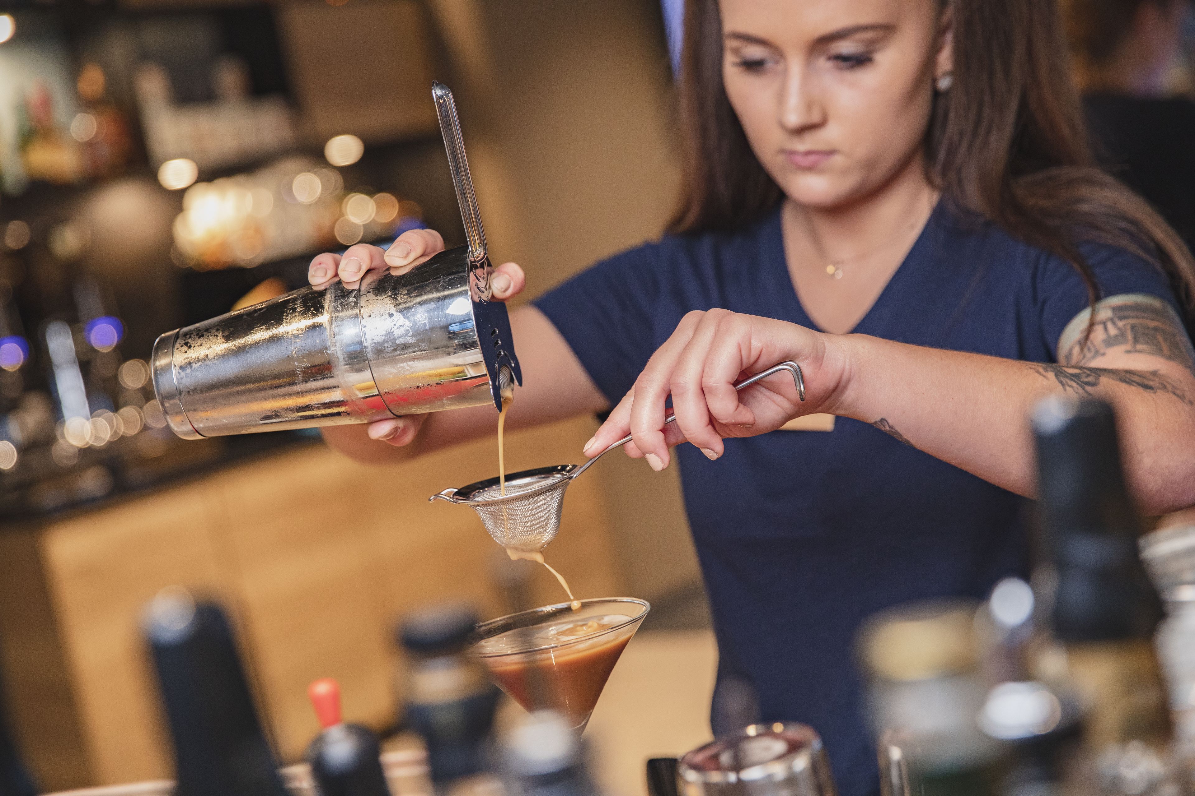 A bartender pouring a drink into a martini glass.