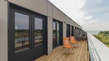 Un edificio moderno con amplios ventanales y una terraza de madera con sillones de descanso.