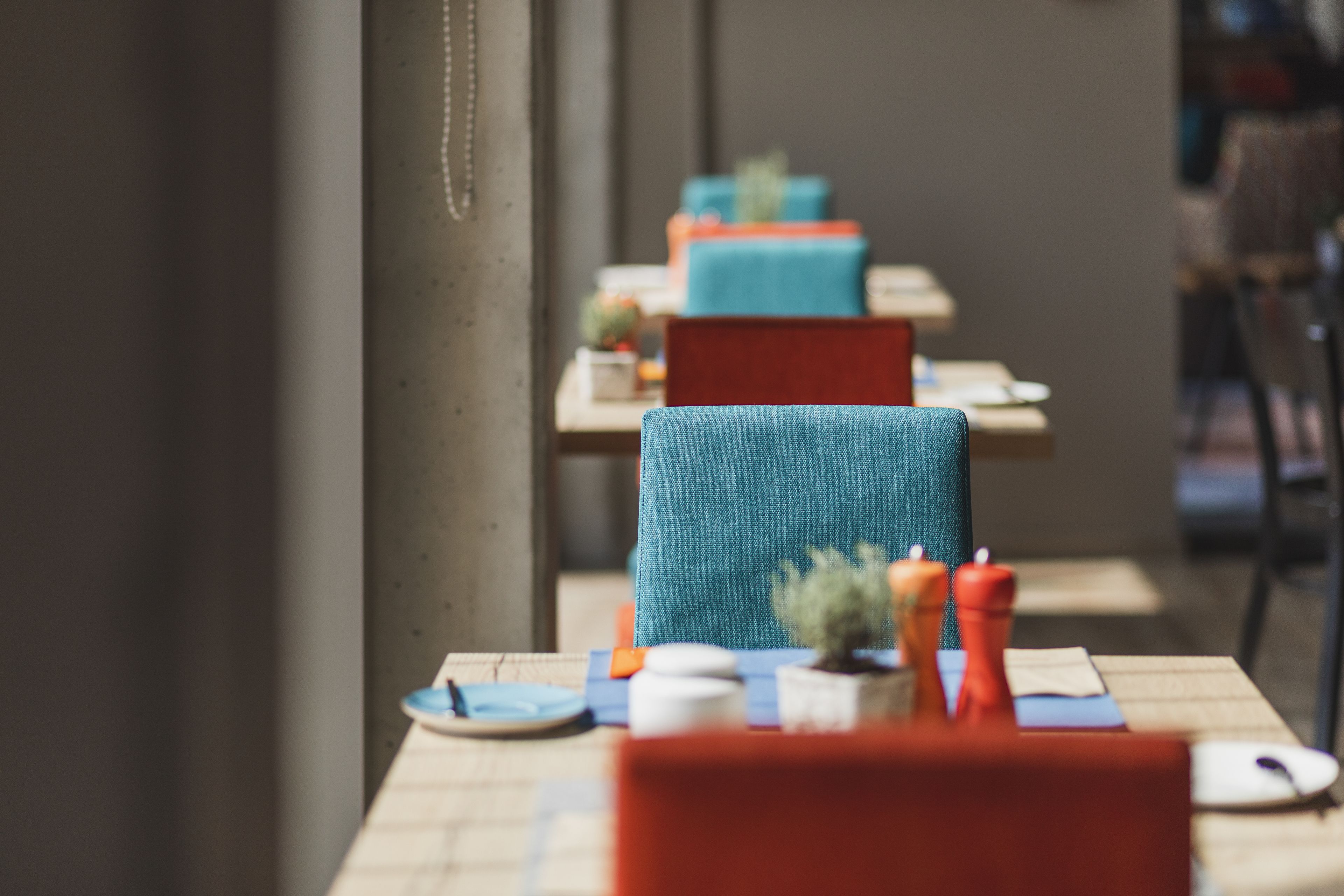 Een eetgedeelte met tafels voor twee personen, met een mix van blauwe en rode stoelen.