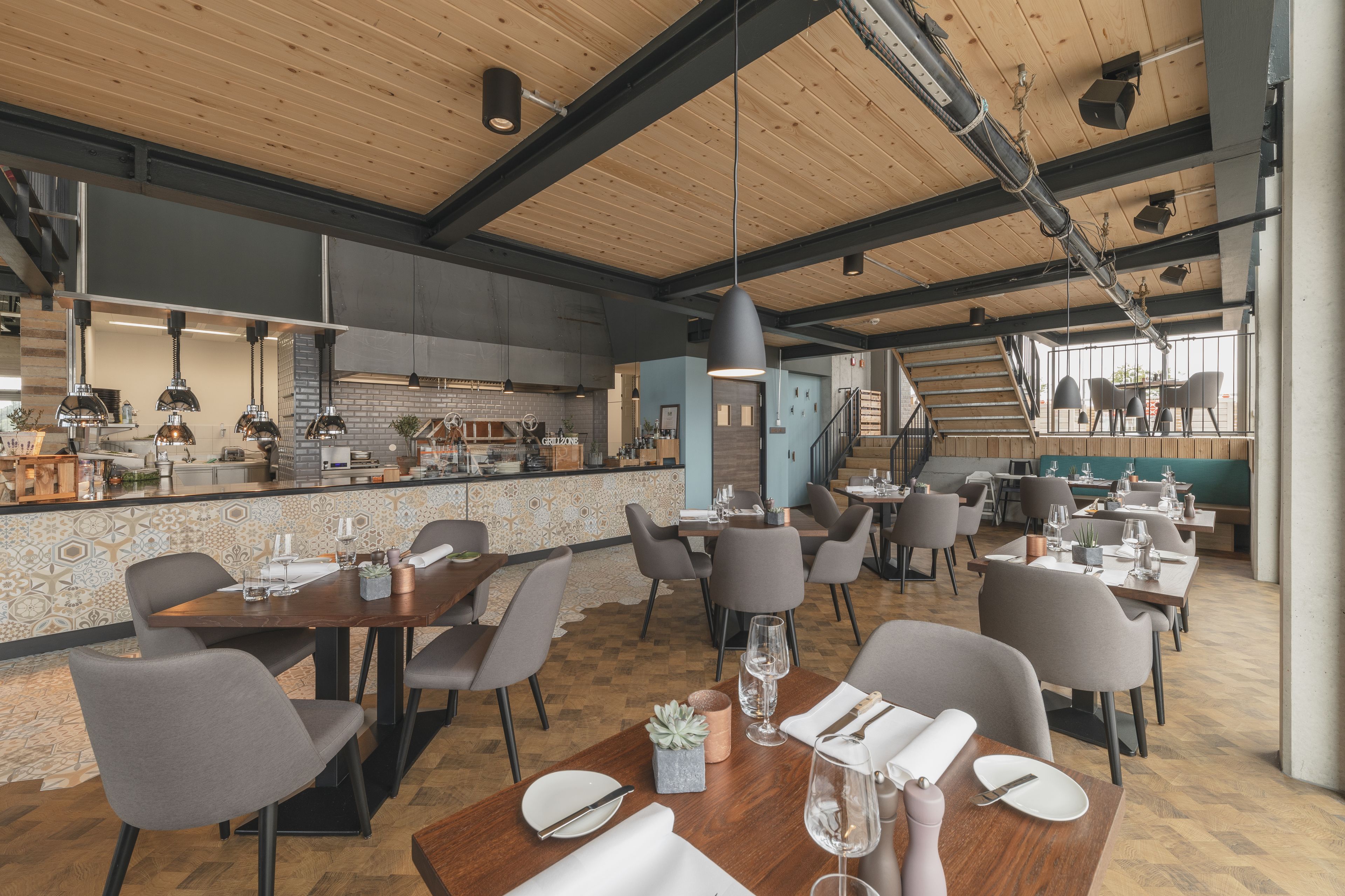 A modern restaurant with wooden ceilings, a bar area, and multiple dining tables with chairs.