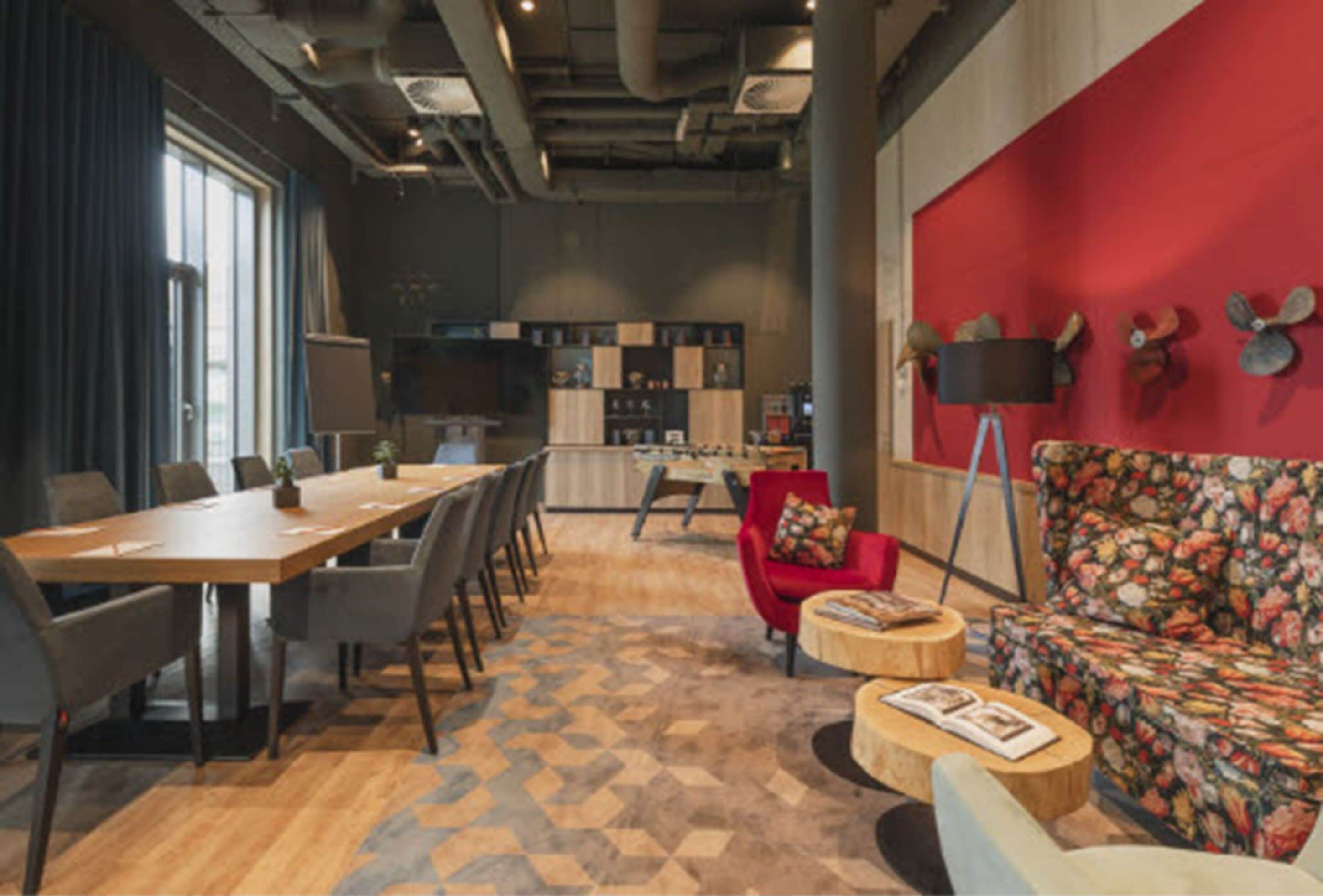 A modern meeting room with a long table, chairs, a red sofa, and a patterned carpet.