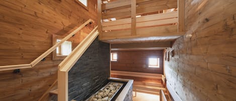 A wooden interior with a stone fireplace, wooden stairs, and a mezzanine level.