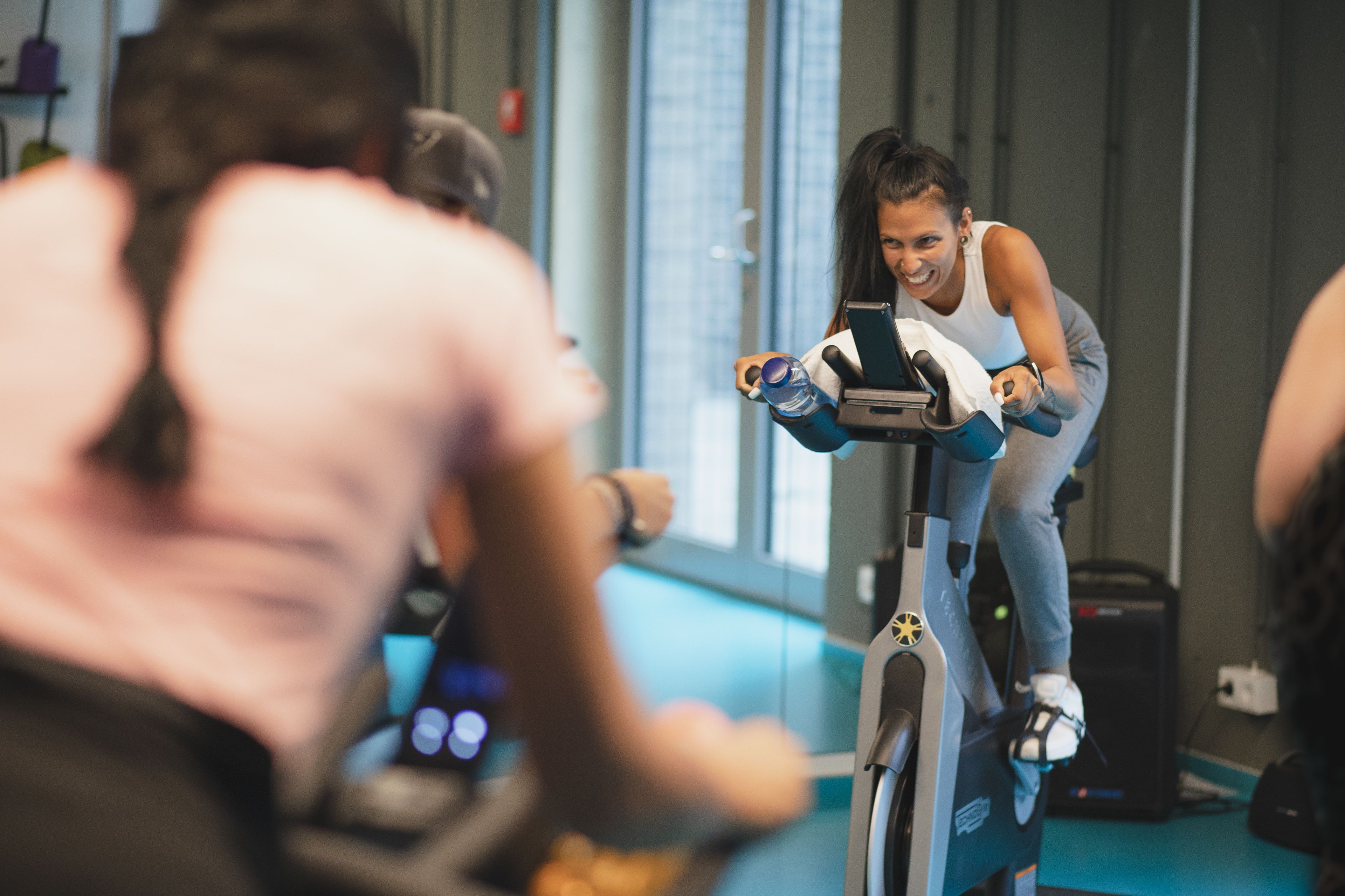 Eine Person fährt in einem Fitnessstudio ein Ergometer und hat eine Wasserflasche sowie eine Smartwatch dabei.