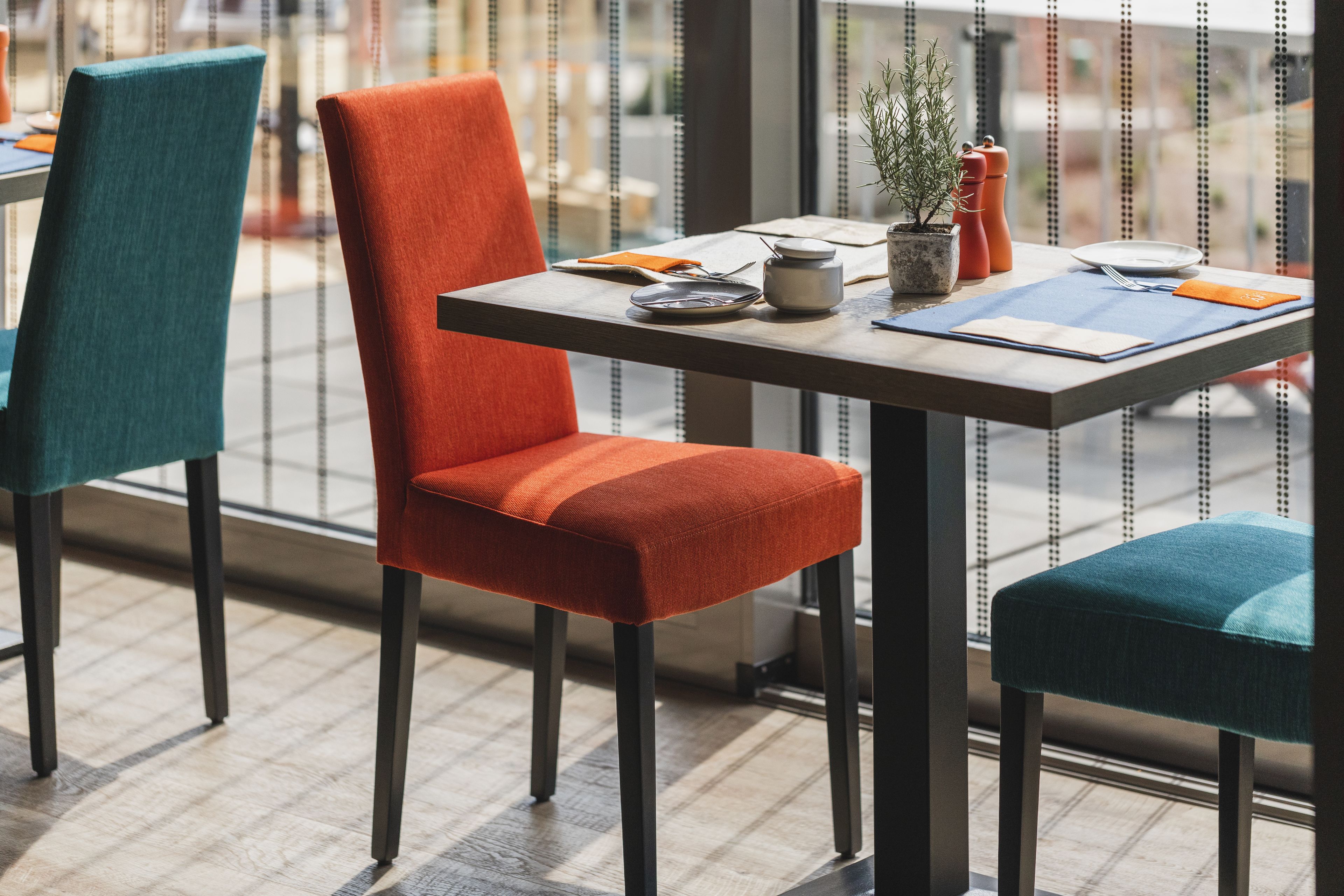 A dining area with a table set for two, featuring a potted plant, a salt and pepper shaker, and a menu.
