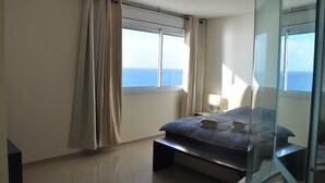 A modern bedroom with a large bed, a bedside table, and a view of the ocean. - Isra Home Luxury Apartment with Sea View (Bat Yam)