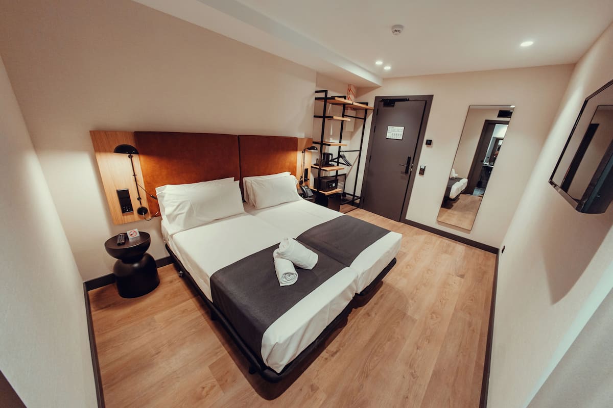 Un cuarto de hotel con una cama grande, una mesita de noche con lámpara, un armario y un espejo en la pared.