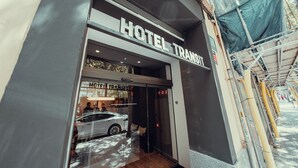 A hotel entrance with a glass door, a sign reading "HOTEL TRANSIT," and a reflection of a white car and people inside. - Hotel Transit (Barcelona)