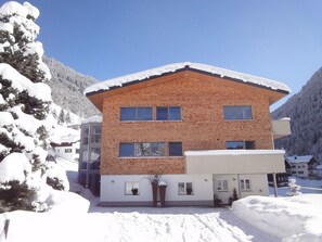 A multi-story building with a brick facade and a sloped roof covered in snow. - Appartements Veronika (Silbertal)