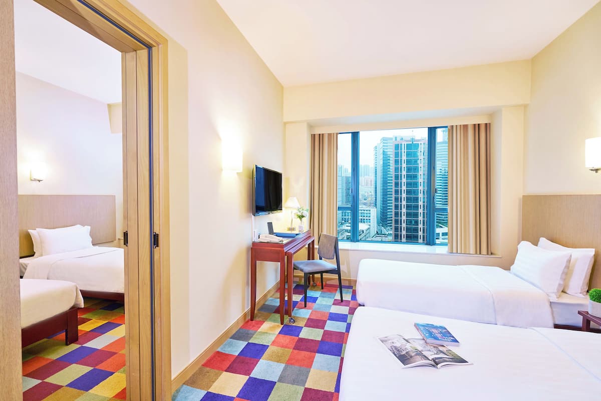 Habitación de hotel con dos camas, un escritorio con silla, televisor y un amplio ventanal con vista a la ciudad.