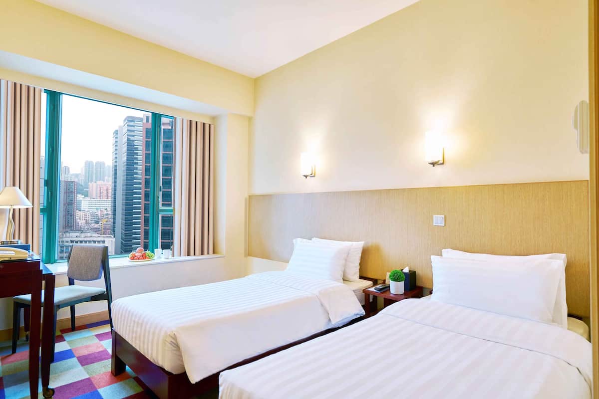 Habitación de hotel con dos camas, un escritorio, una silla y una ventana con vistas a la ciudad.