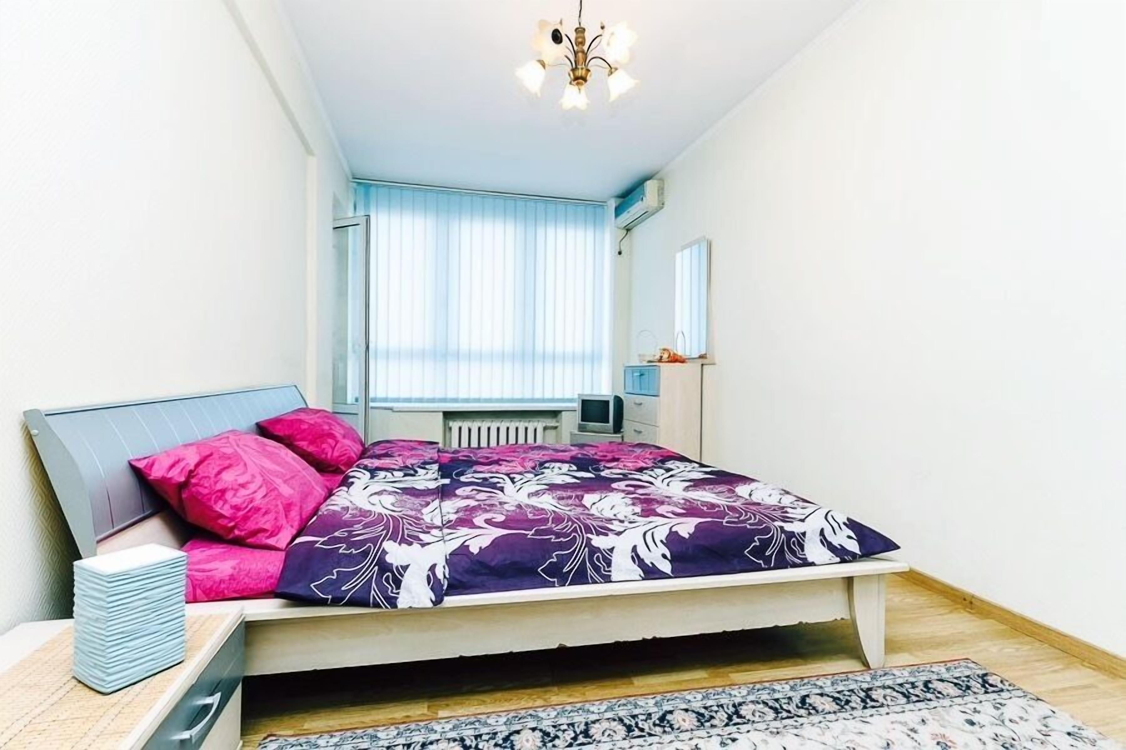 A bedroom with a bed, a dresser, a TV, and a window with blinds.