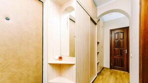 A narrow hallway with wooden flooring, a wooden door at the end, and a small shelf with a red object.