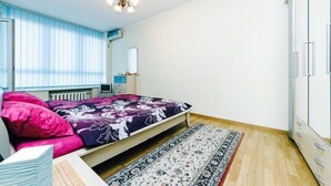 A bedroom with a bed, a desk, a chair, a wardrobe, and a window with blinds.