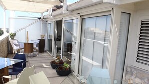 Un balcon avec une table en verre, des chaises, des plantes en pot et une porte-fenêtre coulissante.