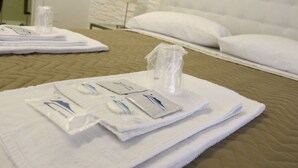 Un lit bien fait, avec des draps blancs, une serviette pliée et un ensemble de produits de toilette disposés sur une couverture de couleur beige.