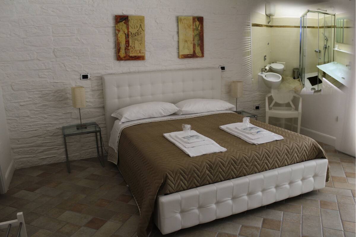 Ein Hotelzimmer mit einem großen Bett, einem Nachttisch, einem Waschtisch, einem Spiegel und einer Toilette.