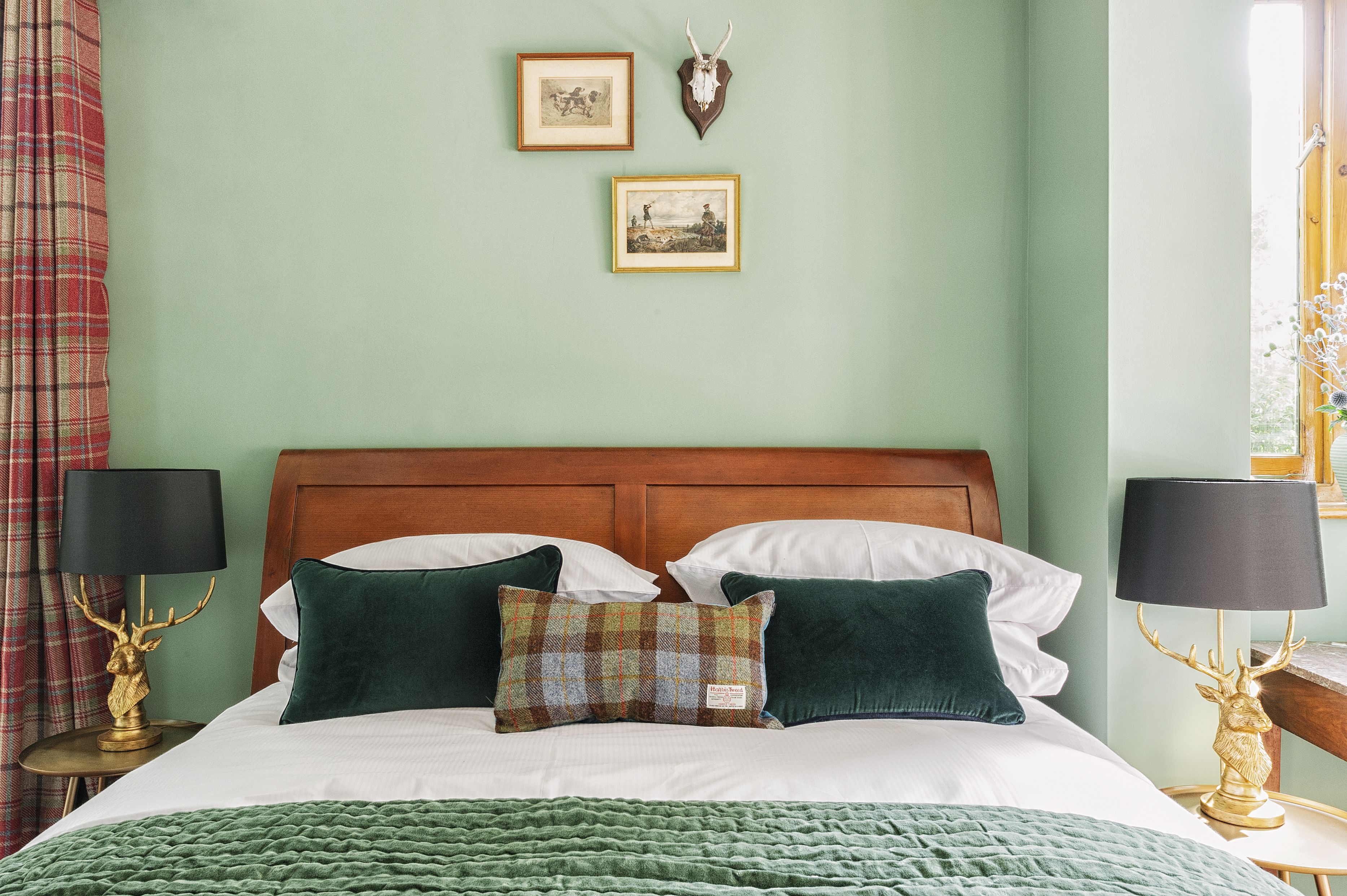A neatly made bed with a green blanket, two pillows, and two bedside lamps with deer head lamps.