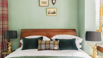 A neatly made bed with a green blanket, two pillows, and two bedside lamps with deer head lamps.