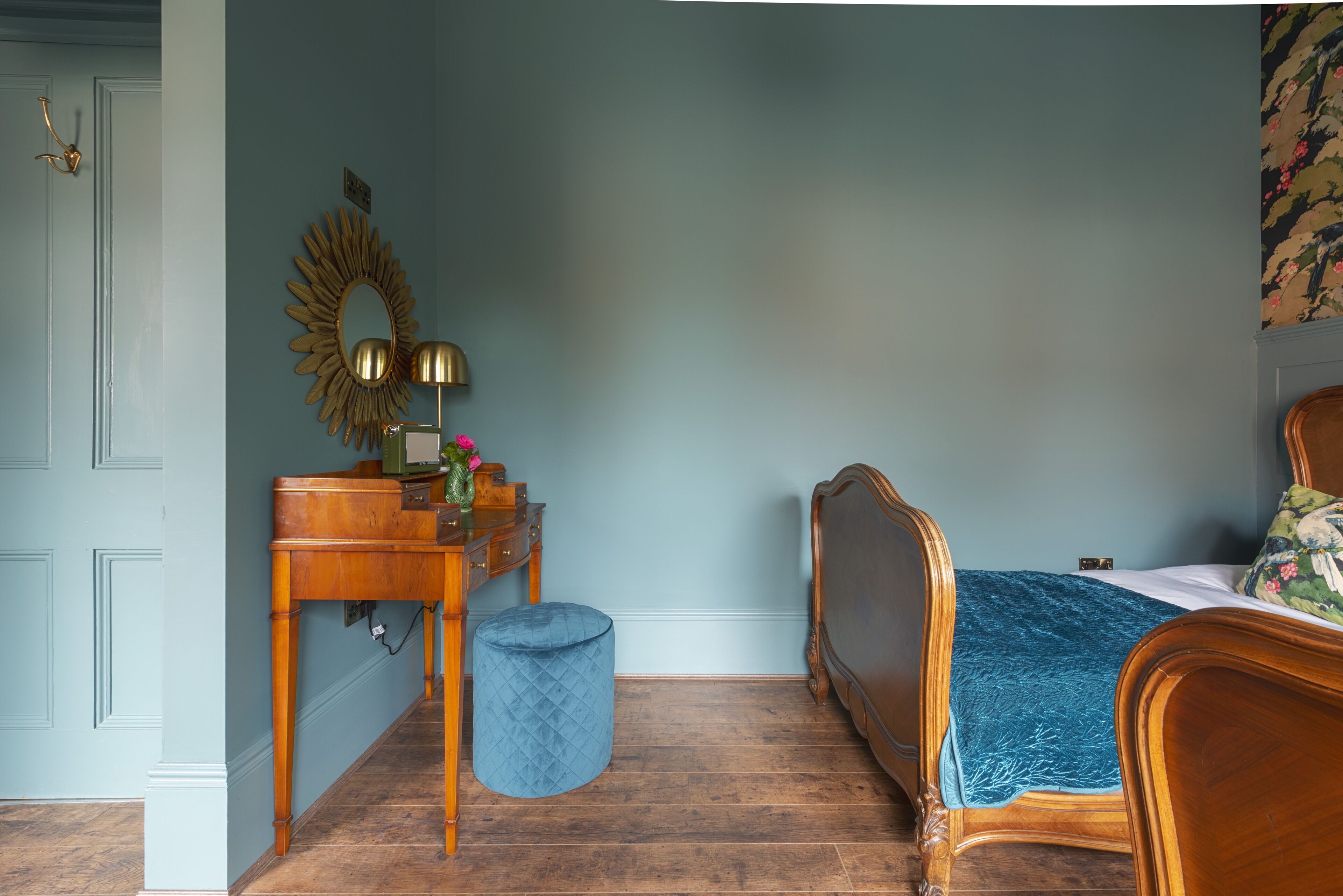 A bedroom with a wooden bed, a dresser, a vanity with a mirror, and a blue ottoman.