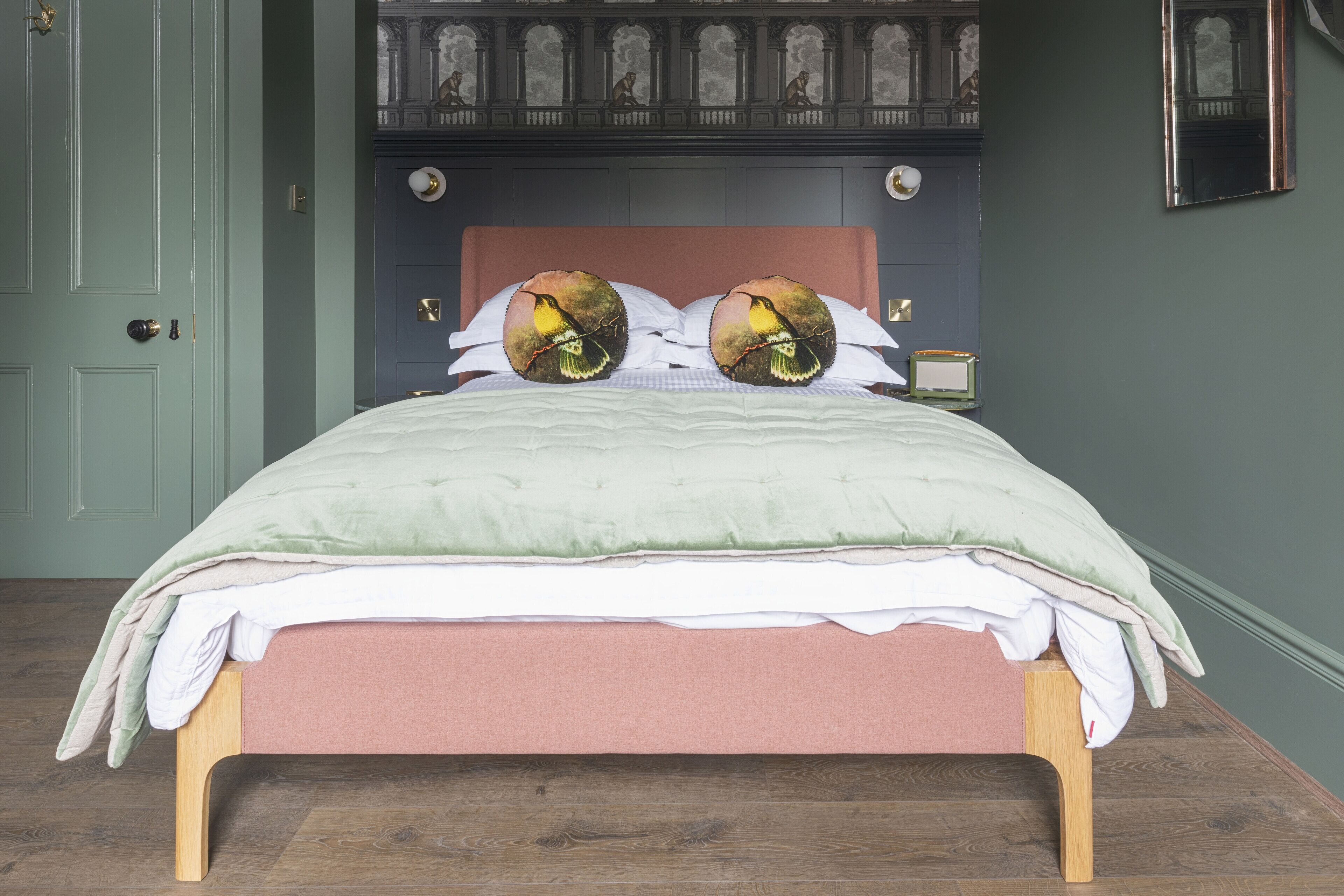 A neatly made bed with a green and pink bedspread, two decorative pillows with bird designs, and a wooden headboard.