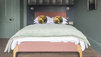 A neatly made bed with a green and pink bedspread, two decorative pillows with bird designs, and a wooden headboard.
