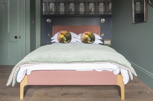 A neatly made bed with a green and pink bedspread, two decorative pillows with bird designs, and a wooden headboard.