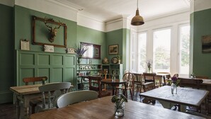 A dining area with wooden tables and chairs, a green wall with a deer head decoration, and a window with natural light. - The Coach House (Derby)
