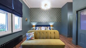 A room with a sofa, two lamps, a patterned wallpaper, and a radiator. - The Coach House (Derby)