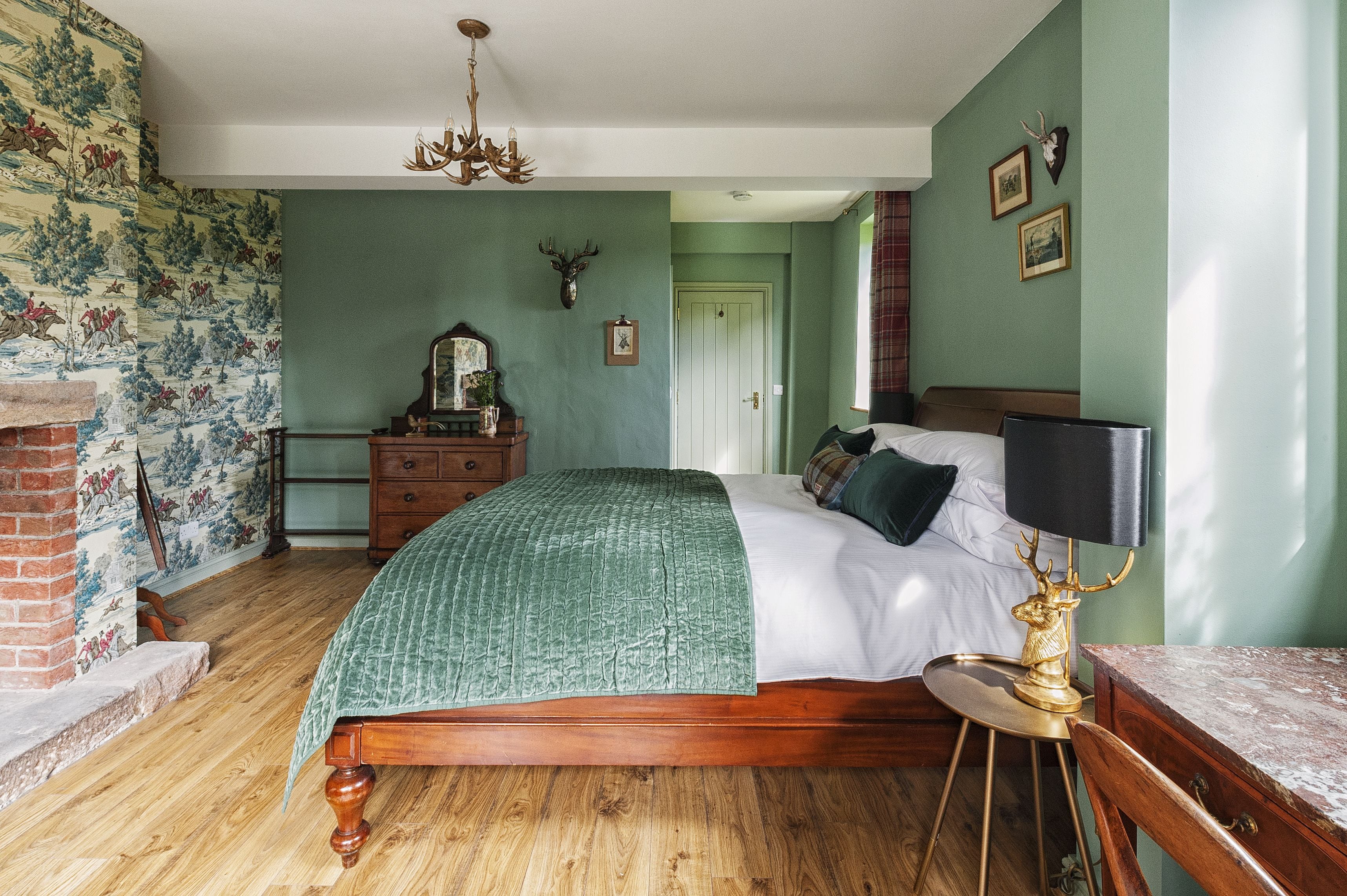 Un dormitorio con cama de madera, paredes verdes, una araña y cuernos de ciervo en la pared.