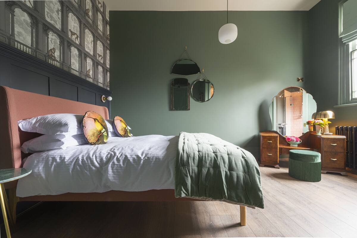 A bedroom with a bed, a dresser, a mirror, and a wall-mounted light fixture.