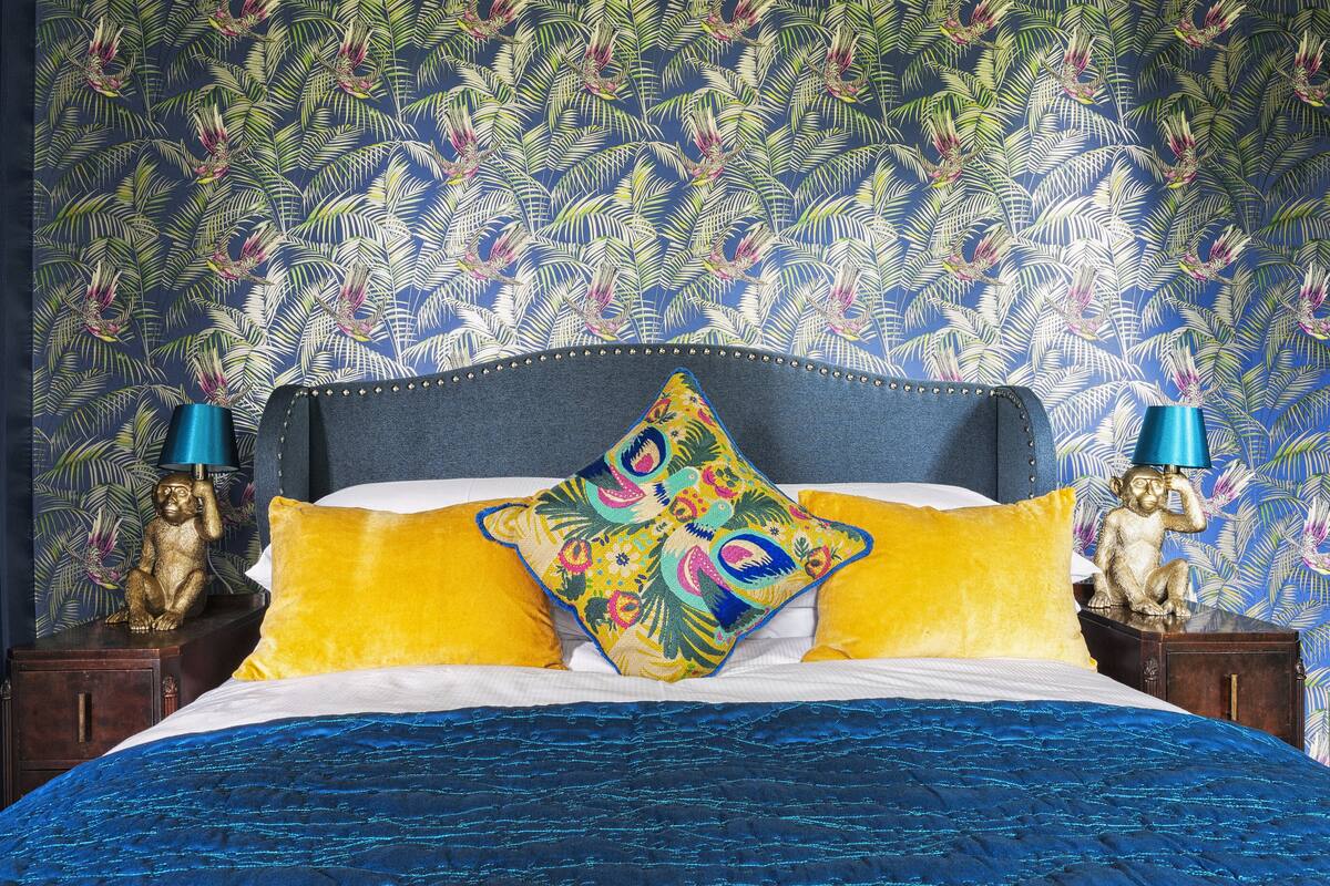 A bed with a blue bedspread, a colorful pillow, and a blue headboard.