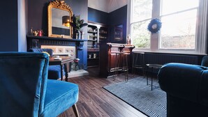 A cozy living room with dark walls, a fireplace, a bar area, and a large window with a wreath. - The Coach House (Derby)