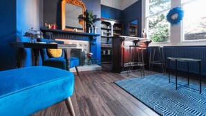A room with a blue sofa, a fireplace, a bar area, and a large window with a wreath. - The Coach House (Derby)
