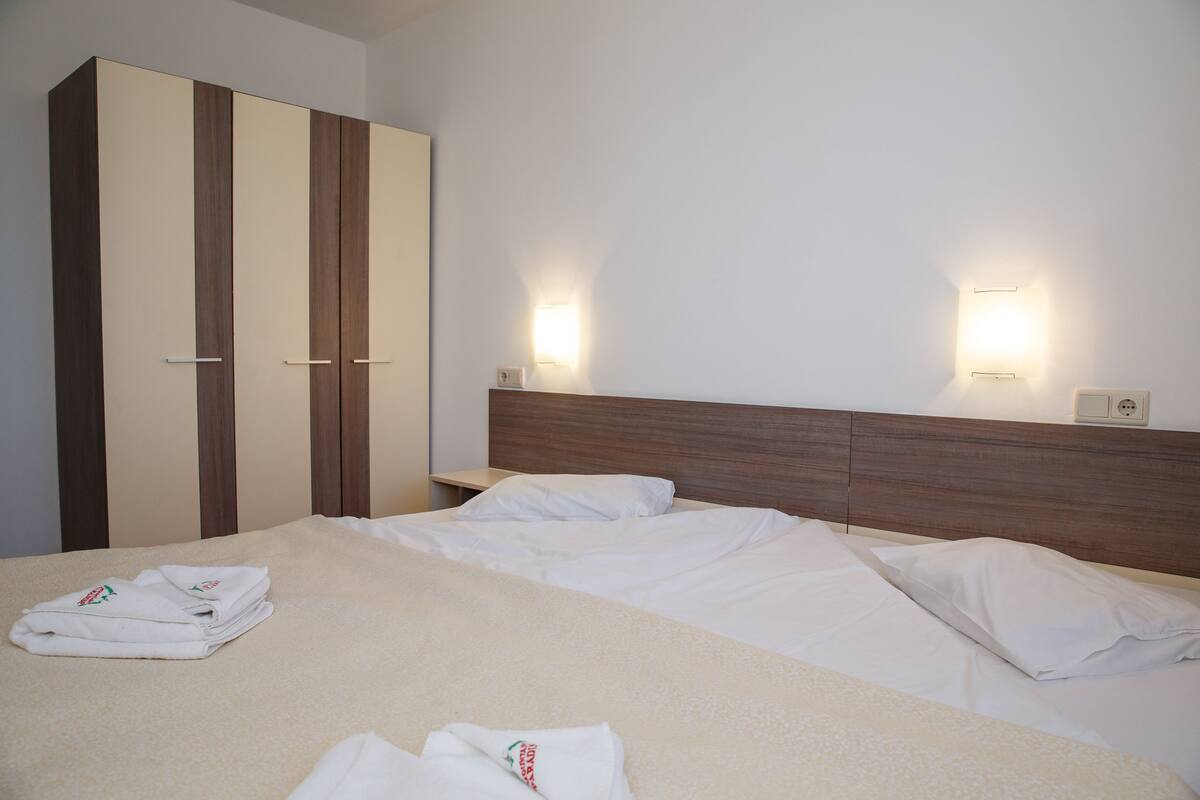 A hotel room with a bed, a wardrobe, and two wall-mounted light fixtures.