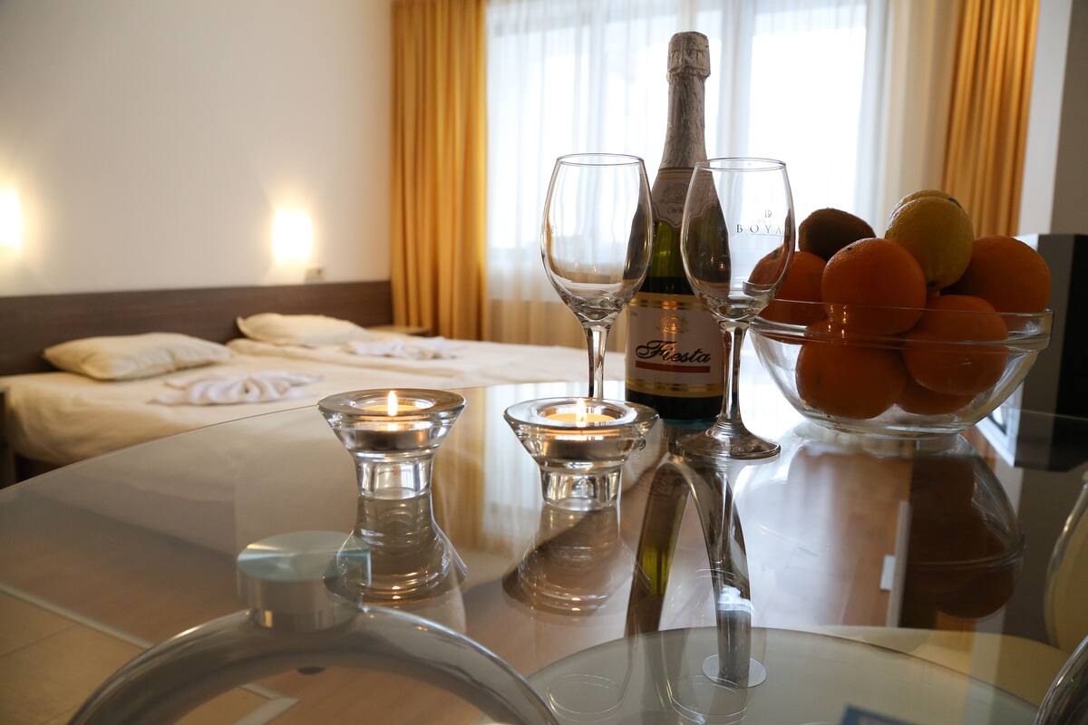 A hotel room with a bed, a table with a bottle of champagne, two glasses, a bowl of oranges, and candles.