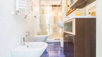Une salle de bain moderne avec un grand lavabo blanc, deux bidet, une douche à parois de verre et un meuble brun.