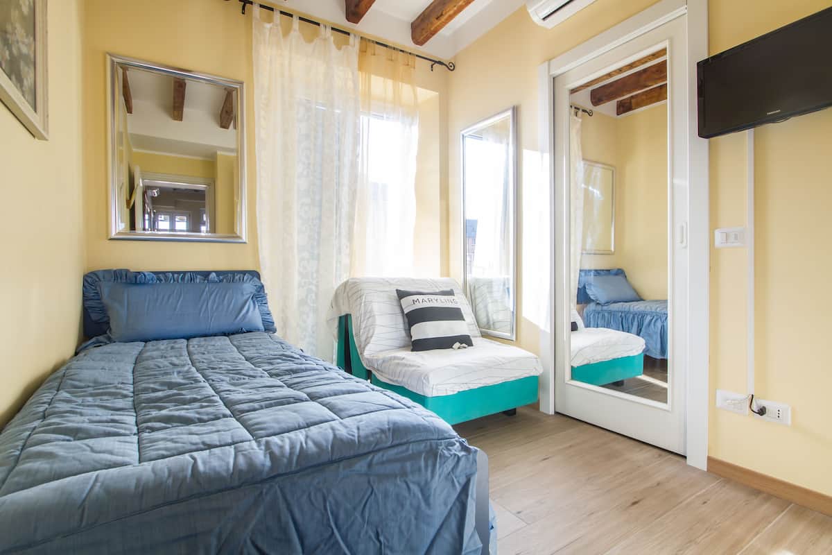 Ein Schlafzimmer mit einem großen Bett, einem kleineren Bett, einem Fenster und einem Spiegel.