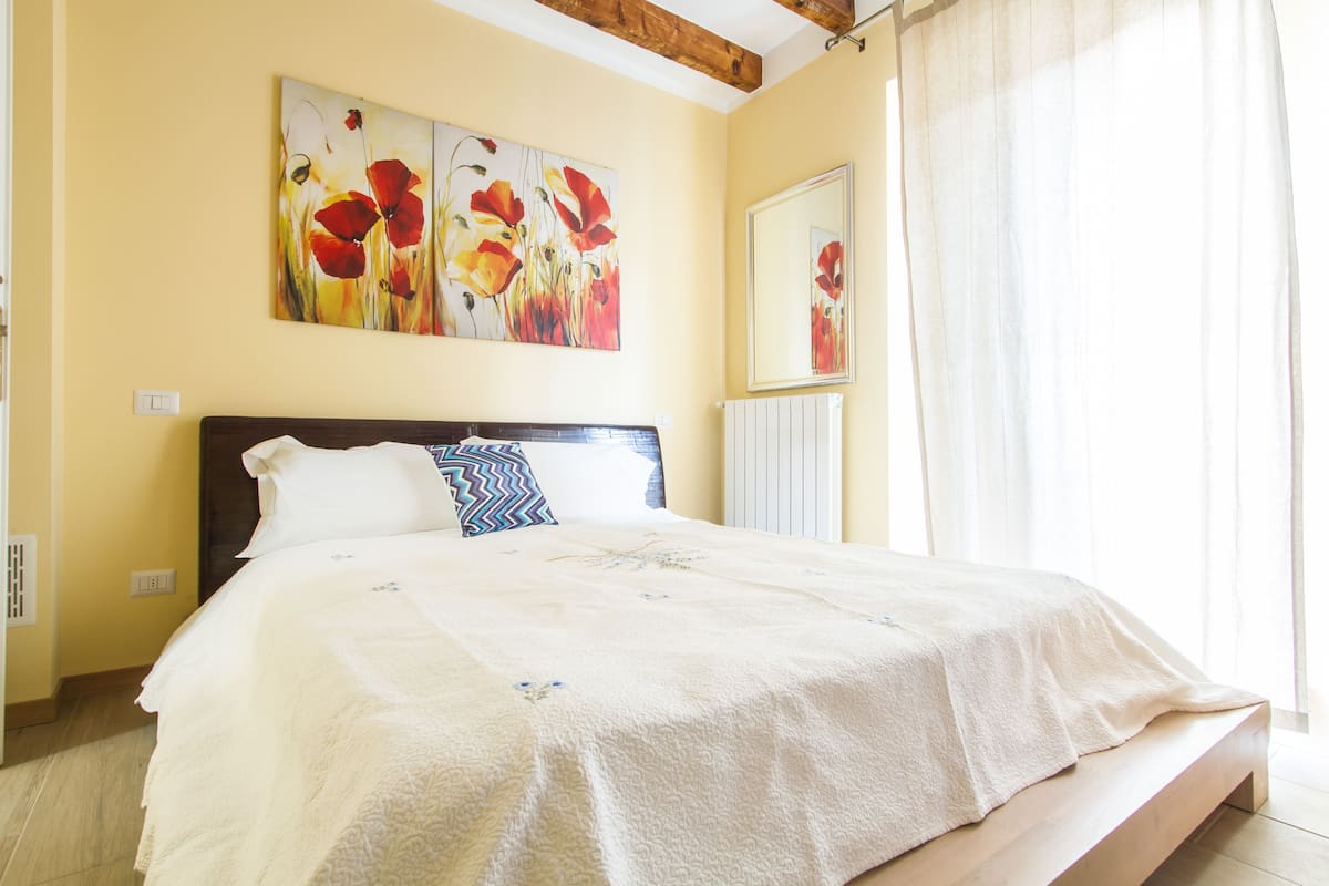 Ein Schlafzimmer mit einem Bett, einem Bild an der Wand und einem Fenster mit Vorhängen.
