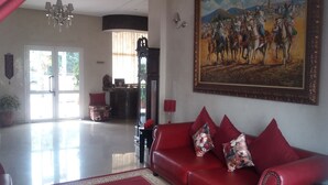 Ampla sala de estar com sofá de couro vermelho, uma pintura grande e um balcão de recepção.