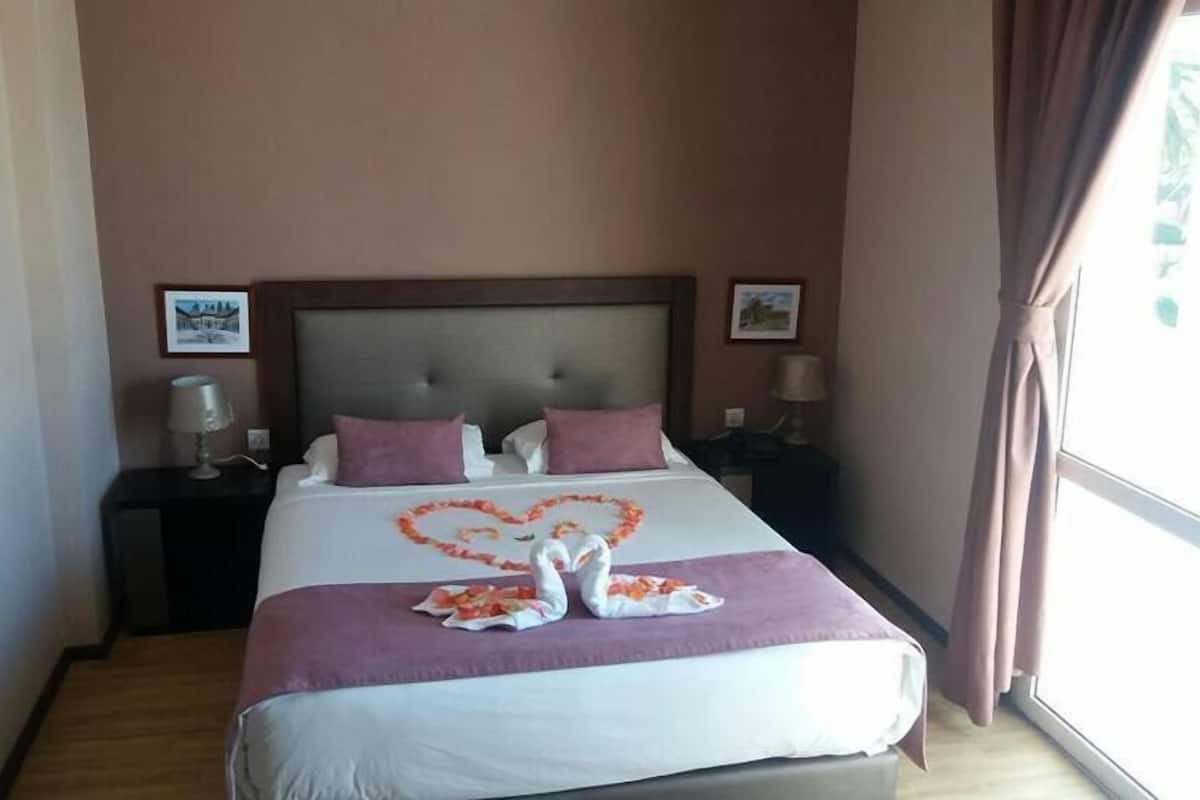 Una habitación de hotel con una cama grande, dos mesitas de noche y un ventanal con cortinas.