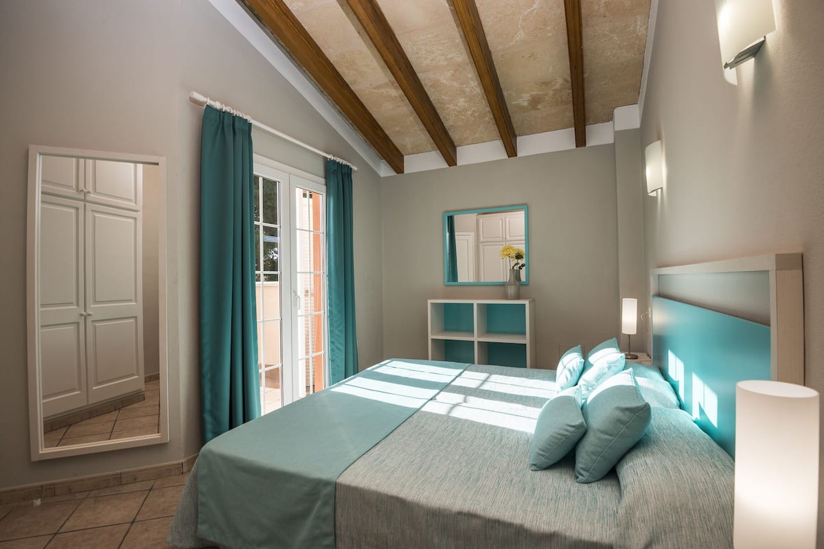 Un dormitorio con una cama, una mesita de noche, un espejo y una ventana con cortinas.