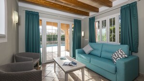 Uma sala de estar com um sofá verde-água, duas poltronas, uma mesa de centro e uma porta de vidro deslizante que dá para uma área externa.