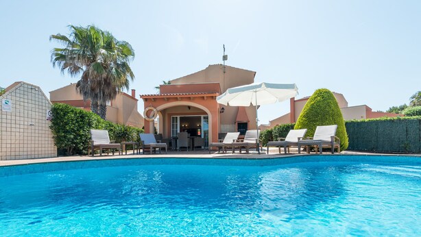 Piscina com espreguiçadeiras e guarda-sóis, uma palmeira e um edifício com fachada azulejada.