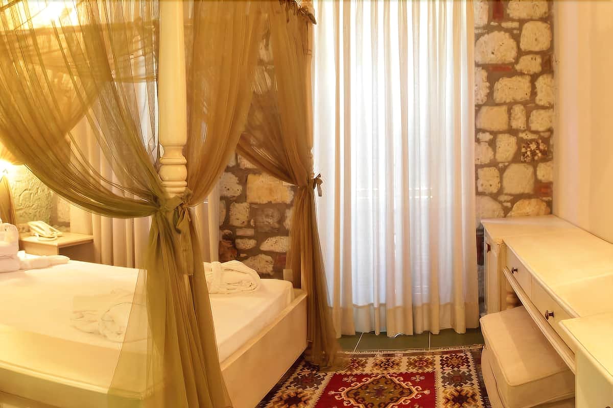 Une chambre à coucher avec un lit, une table de chevet, une lampe, un mur en pierre et une fenêtre avec des rideaux.