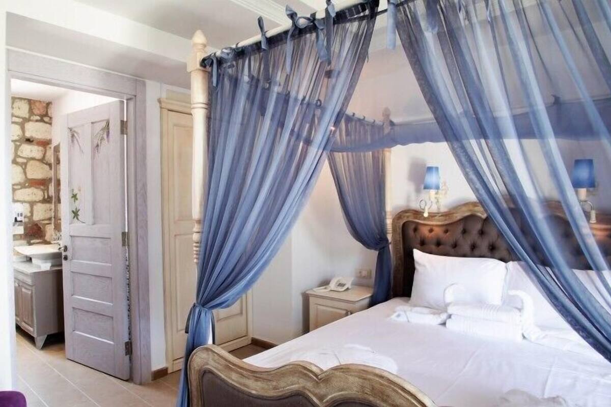 Une chambre à coucher avec un lit à baldaquin, un mur en pierre et une salle de bain visible à travers une porte ouverte.