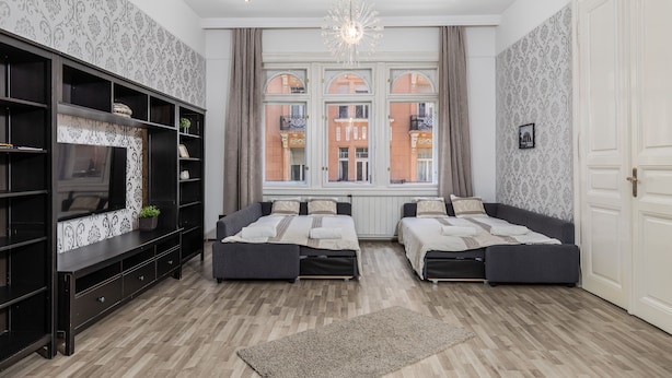 Et moderne værelse med to senge, et fjernsyn og et stort vindue med udsigt til bygninger.