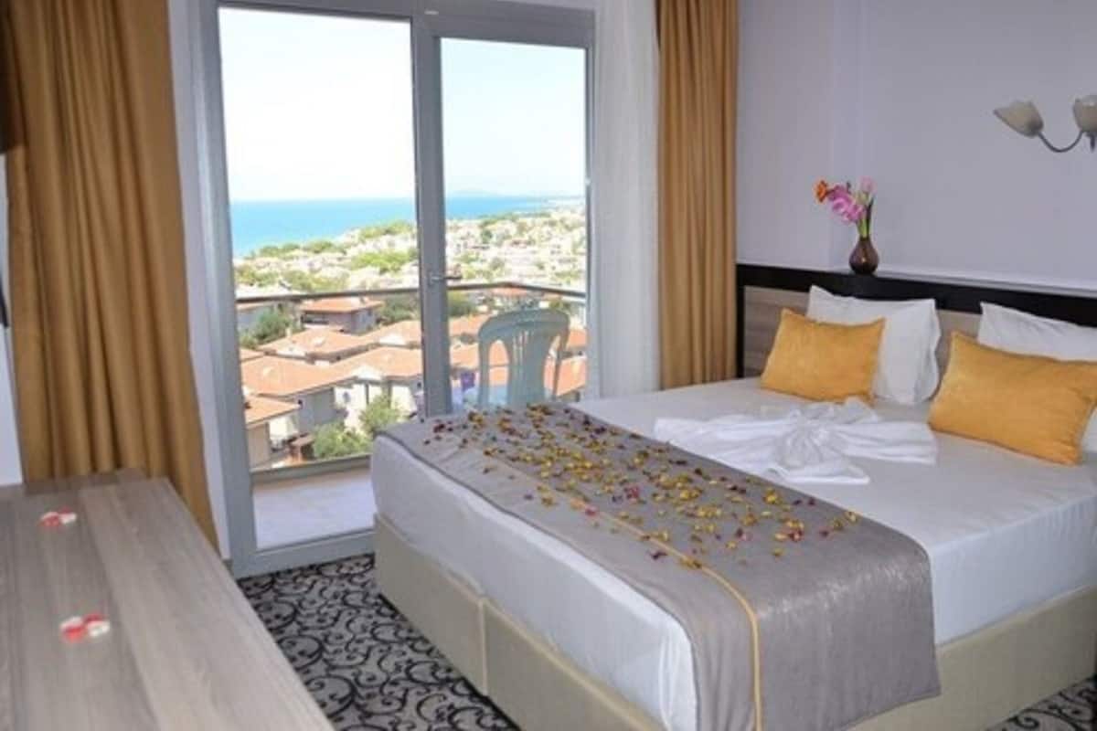 A hotel room with a bed, a table, and a view of the city through a large window.