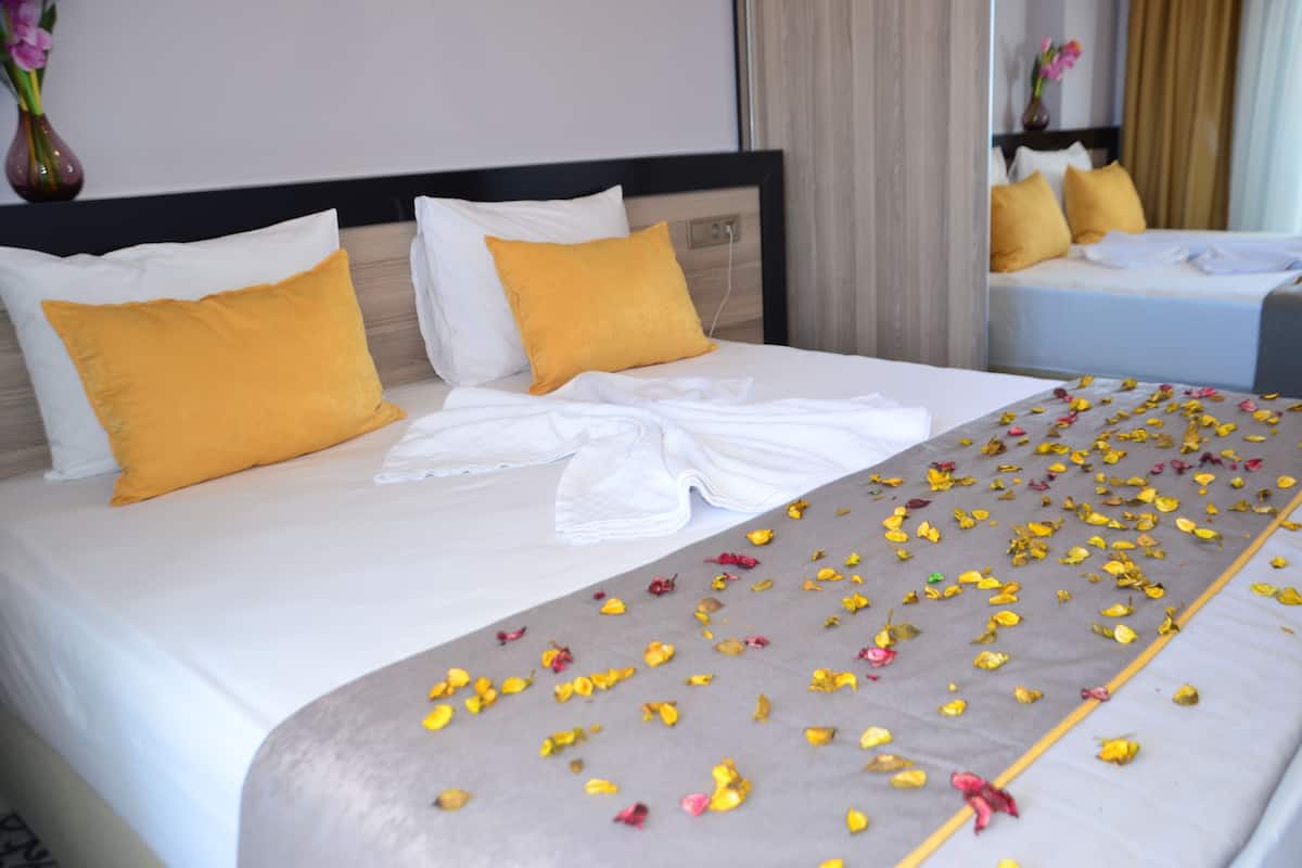 A neatly made bed with yellow and white pillows, a white towel, and scattered flower petals.